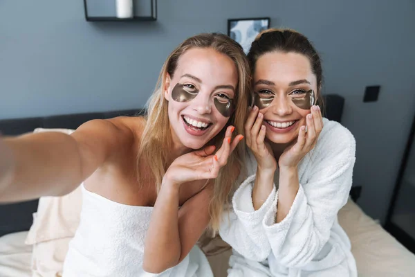 Tevreden jonge vrouwen verzorgen hun huid met onder de ogen vlekken. — Stockfoto