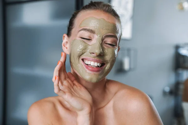 Jovem mulher em casa após spa cuidando de sua pele com máscara facial . — Fotografia de Stock