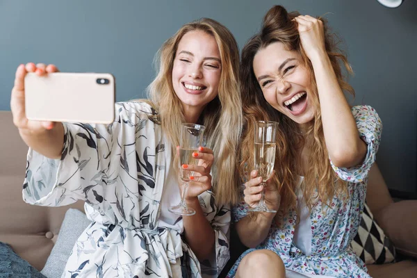 Mignonnes femmes optimistes à la maison boire du champagne prendre selfie par téléphone mobile . — Photo