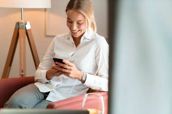 Wanita bisnis cantik pirang yang ceria duduk di dalam ruangan di kafe menggunakan ponsel . — Stok Foto