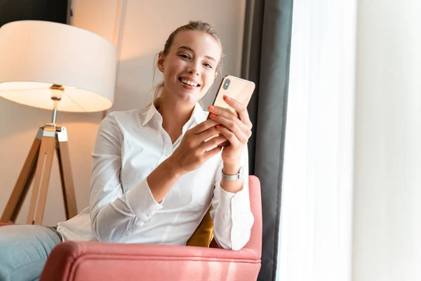 Cheery pretty blonde business woman sit indoors in cafe using mobile phone.