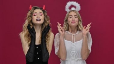 Melek ve şeytan kızlar kırmızı duvar arkasında izole edilmiş karnaval kostümleri içinde dua ediyorlar.
