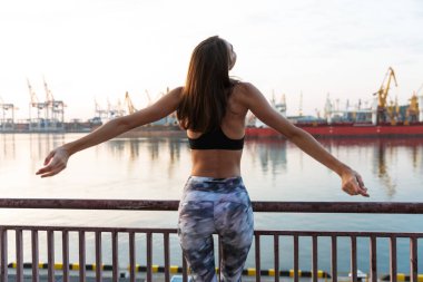 Görüntü arkadan geliyor. Spor yaparken trabzanın yanında duran sportif kadın.