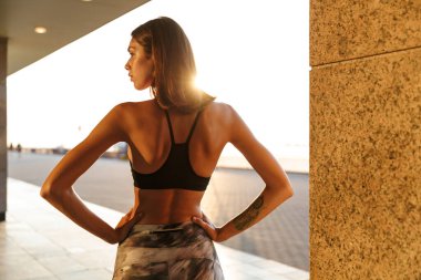 Elleri belinde duran genç bir kadının görüntüsü.