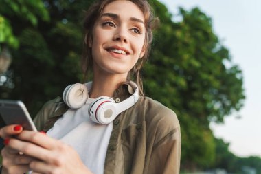 Gülümseyen bir kadının resmi. Elinde akıllı bir telefon, yeşil bir peni ile yürüyor.