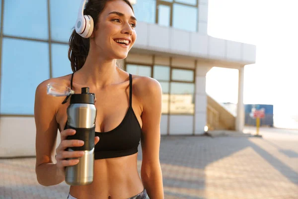 Imagen de una mujer sonriente y complacida usando auriculares y agua potable — Foto de Stock