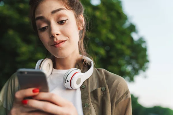 Imagen de una joven sosteniendo un smartphone y caminando en verde par — Foto de Stock