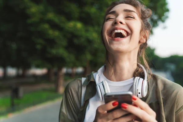 Imagen de una mujer riendo sosteniendo un smartphone y caminando en verde — Foto de Stock