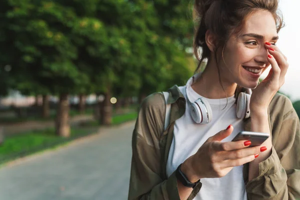 Imagen de una mujer alegre sosteniendo un smartphone y caminando en verde — Foto de Stock