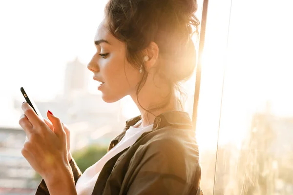 Image of pleased woman in earpods holding smartphone at terrace — Stock Photo, Image