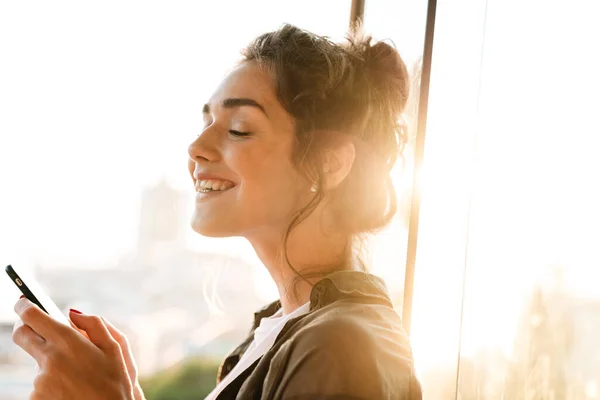 Imagen de mujer feliz en auriculares sosteniendo teléfono inteligente en la terraza ou — Foto de Stock