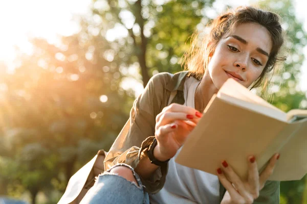 Εικόνα της νεαρής γυναίκας χαμογελώντας και διαβάζοντας το βιβλίο στο πράσινο πάρκο — Φωτογραφία Αρχείου