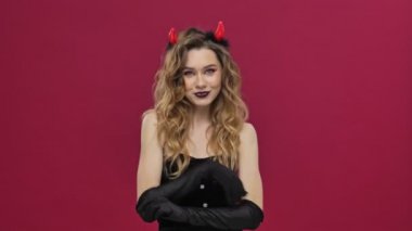 Happy cheery positive devil woman in carnival costume is waving to the camera isolated over red wall background