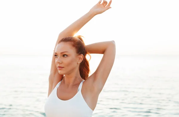 Bella giovane rossa donna sportiva fare esercizio di stretching all'aperto in spiaggia al mattino . — Foto Stock