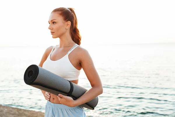 Immagine di giovane donna atletica che tiene il tappetino di yoga mentre fa worko — Foto Stock