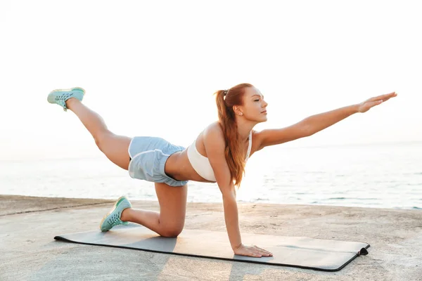 Tamelijk sterk verbazingwekkend mooi jong roodharige sport vrouw maken yoga oefening buiten op het strand in de ochtend. — Stockfoto