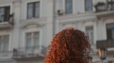 Excited beautiful young redhead curly woman smiling and spinning around while walking at the street