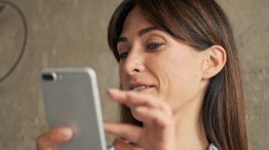 Evde otururken akıllı telefon kullanan ve gülümseyen genç iş kadınının yakın görüntüsü