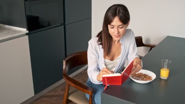 Atractiva Joven Mujer Escribiendo Cuaderno Desayunando Mientras Está Sentada Cocina — Vídeo de stock