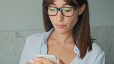 Evde akıllı telefon kullanırken gülümseyen genç ve mutlu bir iş kadını.