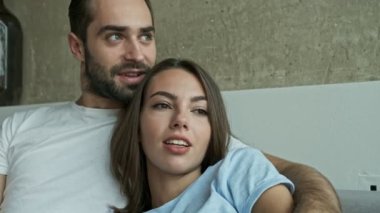 Evdeki kanepede oturup pencereye bakarken kucaklaşan ve konuşan sevimli genç çiftin yakın görüntüsü.