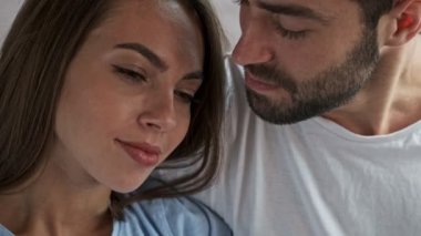 Çekici genç bir kadın erkek arkadaşının omzunda uyanıyor ve evde dinlenirken ona gülümsüyor.