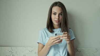 Şirin, neşeli, esmer bir kadın. Evde duvarın yanında durup, akıllı telefondan sohbet ederken gülümsüyor ve gülüyor.