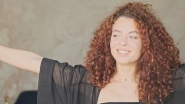 İpek bornozlu, sevimli, neşeli, genç bir kadın. Perdeleri açıyor ve sabahları evdeki pencereye bakıyor.