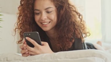 İç çamaşırlı, ipek bornozlu mutlu, genç bir kadın. Sabahları yatakta yatarken gülümsüyor ve akıllı telefondan sohbet ediyor.