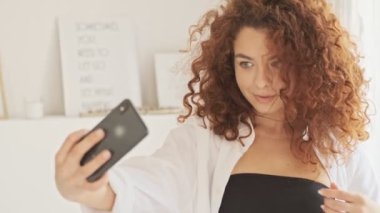 Beyaz tişörtlü, tatlı, mutlu, genç bir kadın. Gülümseyip saçını düzeltirken, sabahları akıllı telefonuyla fotoğraf çekiyor.