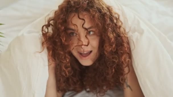 快乐嬉闹的红头发年轻女人躺在床上 从毯子下走了出来 — 图库视频影像