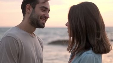 Çekici, mutlu genç çiftin yan görünüşü. Birbirlerine bakıyorlar ve birbirlerine gülümsüyorlar. Deniz kenarında vakit geçiriyorlar.