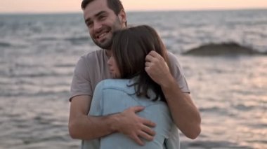 Yakışıklı, genç, sakallı adam kız arkadaşına sarılıyor ve deniz kenarında dinlenirken saçlarıyla oynuyor.
