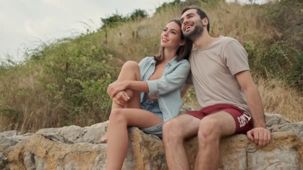 海の近くの丘の上に座っている間 幸せな美しい若い素敵なカップルが抱き合って空を見て — ストック動画