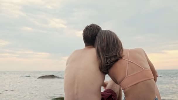 一对年轻貌美的情侣坐在山上观赏大海的背影 — 图库视频影像