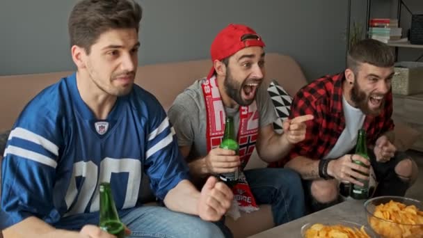 ビールを飲みながら アパートでスポーツを見ながら 3人の楽しい男性ファンが喜びと叫び — ストック動画