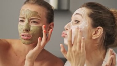 Yüzlerinde maske olan iki güzel gülümseyen kız evde poz verip eğleniyorlar.