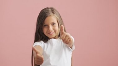 Gülümseyen küçük kız pembe arka planda baş parmak işareti gösteriyor.