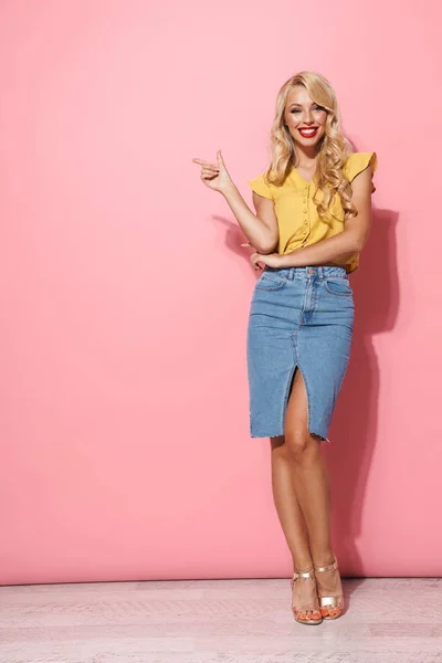 Cheerful young blonde woman posing isolated over pink wall background pointing. — Stock Photo, Image