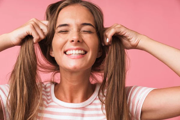 Κοντινό πλάνο της χαρούμενης χαριτωμένης γυναίκας που φοράει ριγέ t-shirt κάνοντας πλάκα με τα μαλλιά της και γκρινιάζοντας — Φωτογραφία Αρχείου