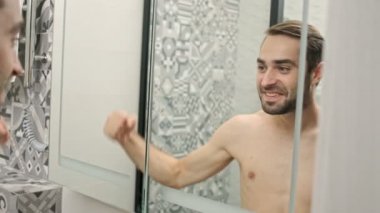 Banyodaki aynaya bakarken kaslarını gösteren ve bağıran neşeli, yakışıklı, sakalsız genç adamın yansıması.