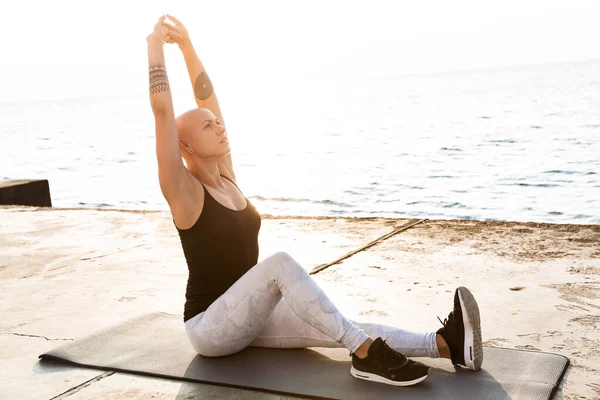 Imagen de una mujer calva y tranquila haciendo ejercicios en la estera mientras hace ejercicio —  Fotos de Stock