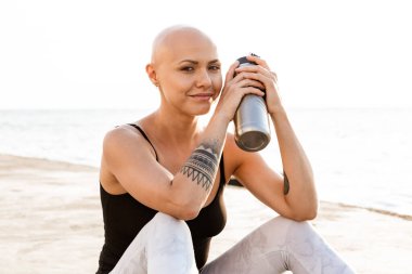 Elinde su şişesi olan gülümseyen kel bir kadın.