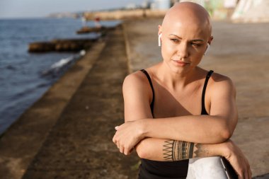 Otururken cep telefonu ve kulaklık kullanan sakin kel kadın görüntüsü