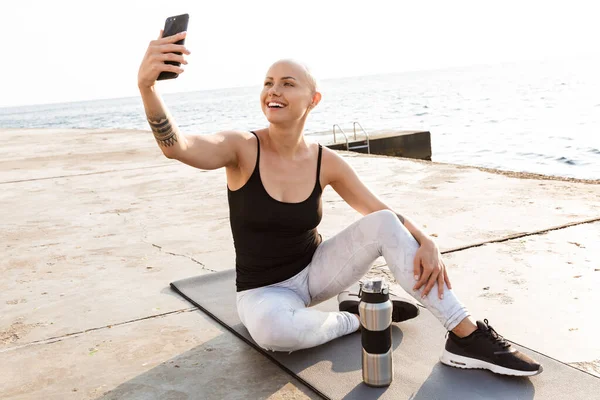 A mosolygó, kopasz nő képe, amint szelfi fotót készít a mobilján — Stock Fotó