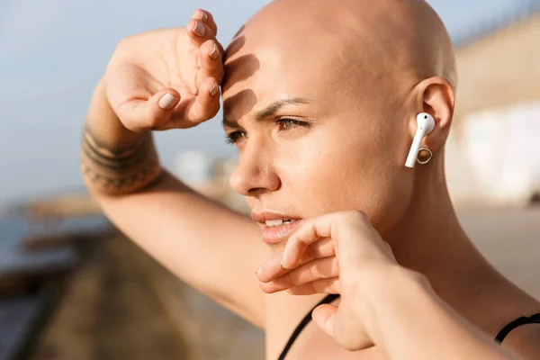 Image closeup pretty bald woman using earphones and looking forward