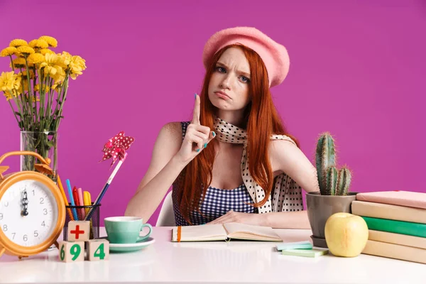 Image of strict teenage girl showing index finger while studying with exercise books