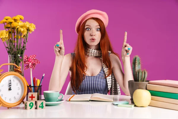 Photo de fille étudiante étonnée pointant les doigts vers le haut tout en faisant des devoirs — Photo