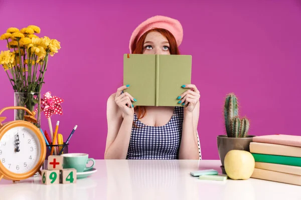 Imagem de menina estudante caucasiana cobrindo seu rosto com livro de diário enquanto sentada na mesa — Fotografia de Stock