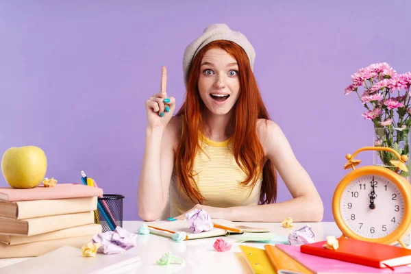 Photo de joyeuse étudiante pointant du doigt vers le haut assise au bureau avec des livres — Photo